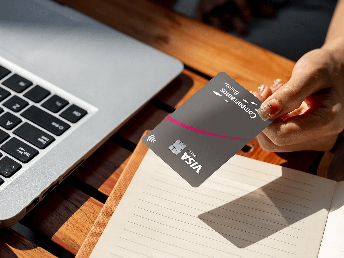 Mano sosteniendo tarjeta compartamos al lado de computador